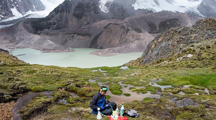 A researcher gathering samples near a beautiful lake by mountains