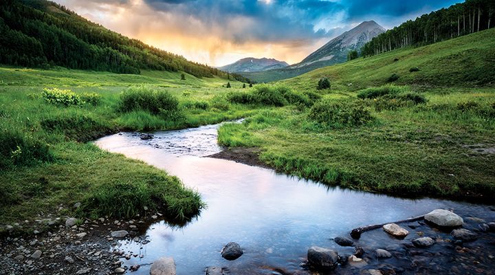 An image of a winding river and a colorful sunset over mountains in the background