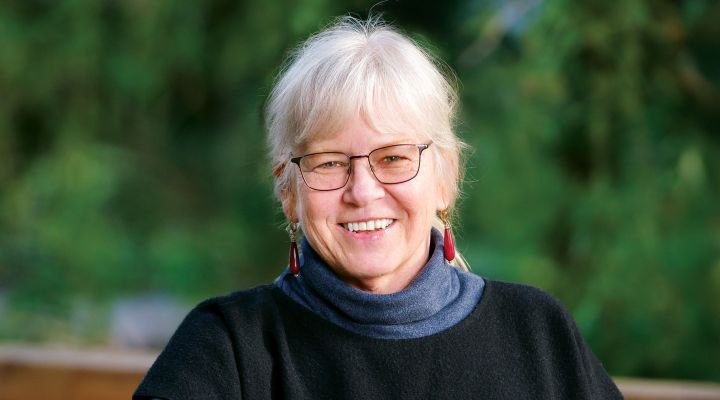 A woman outside with green trees behind her